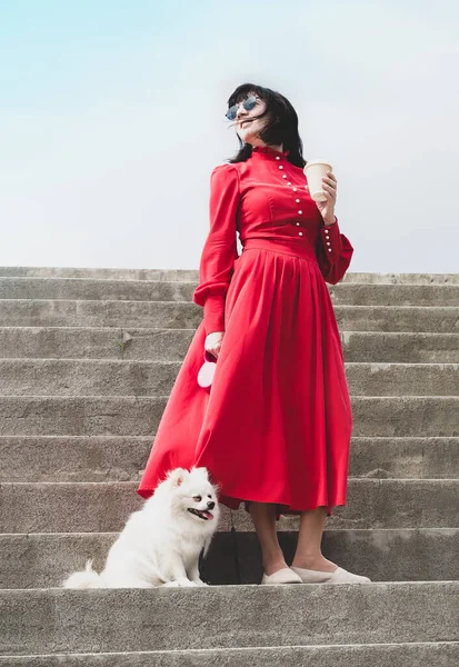 Eine Frau im roten Kleid mit einer Tasse Kaffee und einem kleinen weißen, flauschigen Hund — Stockfoto