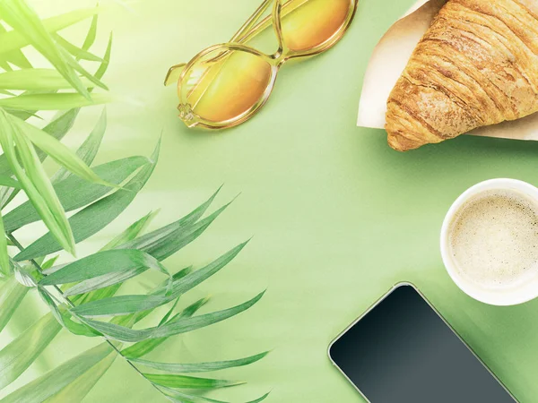 Taza de papel de café, croissant, teléfono, gafas de sol y hojas de palma — Foto de Stock