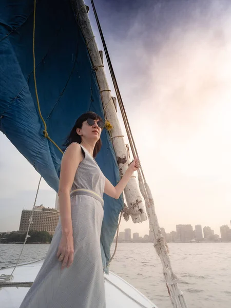 Una mujer caucásica en un vestido azul y gafas de sol se encuentra en un barco de felucca Fotos De Stock