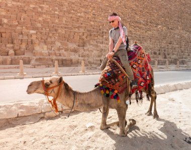 Bir turist devenin üstünde Giza 'daki piramitlerin arka planında poz veriyor.