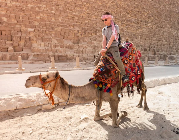 Bir turist devenin üstünde Giza 'daki piramitlerin arka planında poz veriyor.