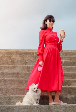 Kırmızı elbiseli bir kadın, bir fincan kahve ve küçük beyaz tüylü bir köpek.