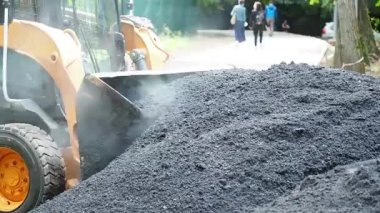 Traktör asfaltı kovaya sokuyor ve onu iş yerine götürüyor.
