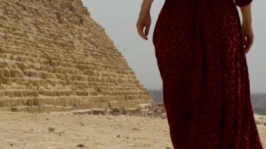 Uzun elbiseli bir kadın Giza piramidinin yanından geçiyor.