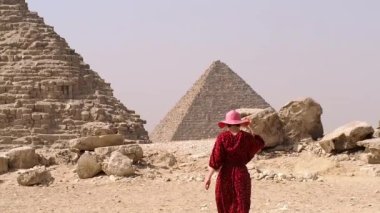 Uzun elbiseli bir kadın Giza piramidinin yanından geçiyor.