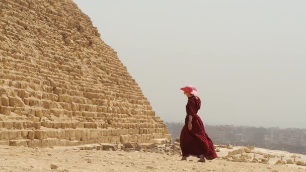 Een vrouw in een lange jurk passeert naast de piramide van Gizeh — Stockvideo