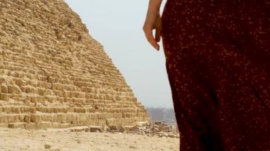 Uzun elbiseli bir kadın Giza piramidinin yanından geçiyor.