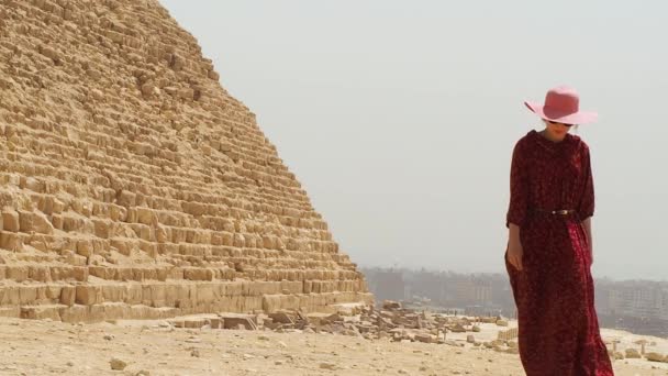 Een vrouw in een lange jurk passeert naast de piramide van Gizeh — Stockvideo