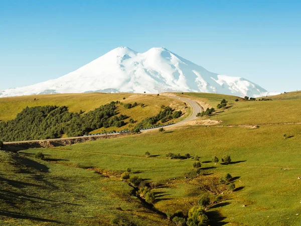 Piękny zakręt drogi przez zielone wzgórza Kaukazu do Elbrus. — Zdjęcie stockowe