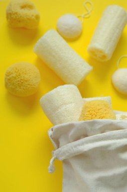 Sıfır atık. Doğal organik hijyen ürünleri. Lif süngeri ve süngerimsi konnyaku parlak sarı bir zemin üzerine pamuk bej bir çantaya konmuş. Makul tüketim konsepti. Temizlik ve sağlık.