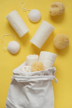Sıfır kayıp. Doğal organik hijyen ürünleri. Lif süngeri ve süngerimsi konnyaku parlak sarı bir zemin üzerine pamuk bej bir çantaya konmuş. Makul tüketim konsepti. Temizlik ve sağlık.