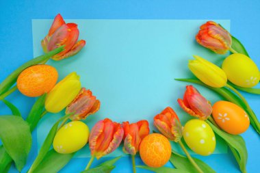 Paskalya tatili. Turuncu ve sarı laleler ve parlak mavi arkaplanlı paskalya yumurtaları. Kopya uzay. Paskalya festivali arka planı 