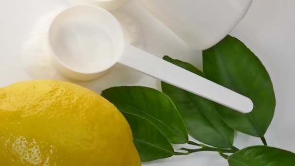 C vitamini tozu. Beyaz plastik kaşık ve kavanozda C vitamini tozu, beyaz arka planda yeşil yapraklı limon meyvesi.. — Stok video