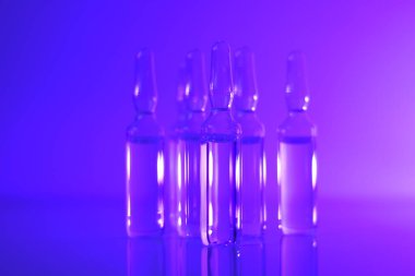 Tıp ve farmakoloji konsepti. Aşı ampulleri. Cam şeffaf ampuller mor ışıkta. Biyoteknoloji ve bilim. Enjeksiyon için çözeltiler.