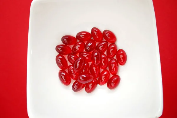 krill oil red gelatin capsules close-up.omega fatty acids.Natural supplements and vitamins.Red capsules with krill oil in a white cup on a bright red background