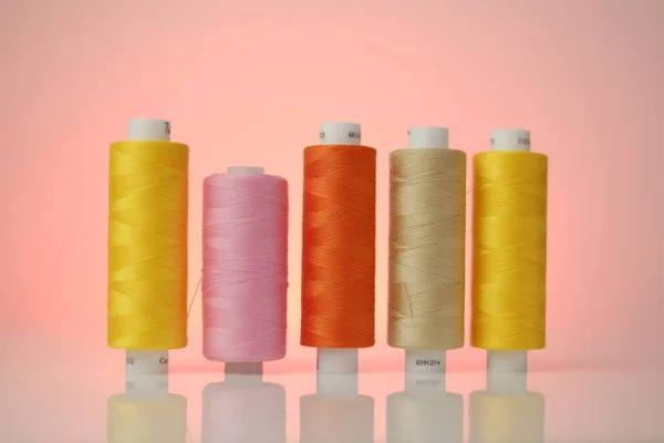Filati per cucire. Set di fili multicolori. Fili gialli, arancioni e rosa su fondo rosa. — Foto Stock