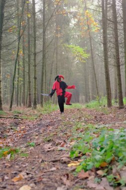  Cadılar Bayramı tatili. Korkunç palyaço. Sonbahar sisli ormanında bıçaklı kötü soytarı. Korkunç soytarı kostümü ve kafatası maskesi. Korku ve korku konsepti. Ormandaki korkunç palyaço.