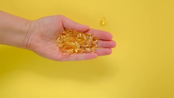 Vitamina D. Cápsulas de gelatina con extracto de aceite de vitamina D en una mano femenina sobre un fondo amarillo. — Vídeo de stock