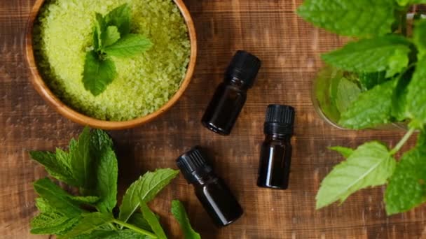 Peppermint essential oil and sea salt with mint extract, peppermint sprigs on brown wooden background.Organic natural eco oils. Natural bio cosmetics and aromatherapy — Stock Video