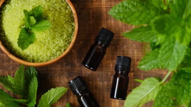 Peppermint oil and sea salt with mint extract, peppermint sprigs on wooden background. Natural bio cosmetics and aromatherapy — Stock Video