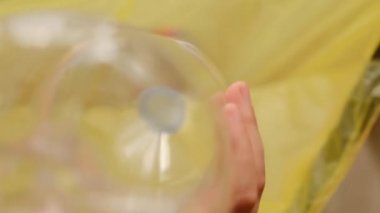 Plastik şişeler. El, plastik şişeyi sarı bir çöp torbasına atar..