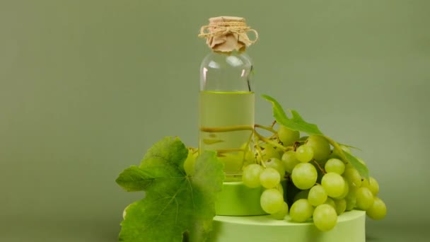 Traubenkernöl. Glasflasche und Bündel grüner Trauben mit Blättern auf grünem Podium auf grünem Hintergrund. Biologisches natürliches Bio-Traubenkernöl — Stockvideo