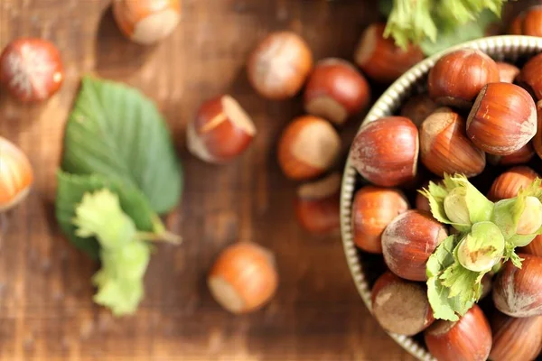 Primeros planos de avellana.Nueces abundantes.Nueces en la mesa.Cosecha de nueces. Placa de frutos secos maduros y frutos secos verdes con hojas sobre fondo de madera —  Fotos de Stock