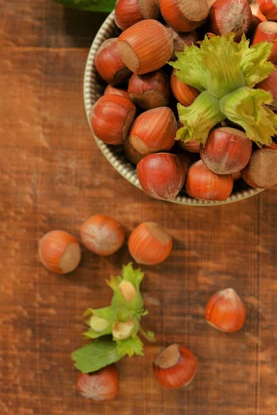 Avellana de primer plano.Nueces abundantes.Nueces en la mesa. Placa de frutos secos maduros y frutos secos verdes con hojas sobre fondo de madera —  Fotos de Stock