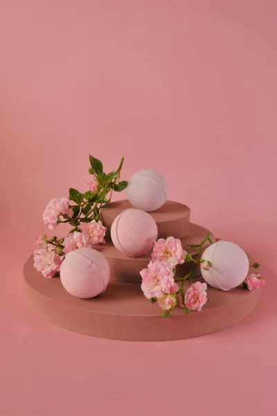 Bombas de banho com extrato de rosa.Bombas de banho rosa e flores rosa rosa no pedestal borgonha em um fundo rosado.Cosméticos veganos orgânicos. Bombas de banho de flor — Fotografia de Stock