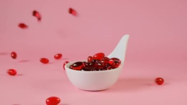 Açık pembe arka planda beyaz seramik kaşıkta kril yağı jelatin kapsülleri. Uçan kapsüller kırmızı kril yağı. Omega yağ asitleri. Doğal takviyeler ve vitamin.