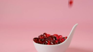 Açık pembe arka planda beyaz seramik kaşıkta kril yağı jelatin kapsülleri. Uçan kapsüller kırmızı kril yağı. Omega yağ asitleri. Doğal takviyeler ve vitamin.