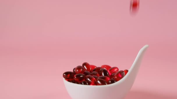 Capsule di gelatina di olio di krill in un cucchiaio di ceramica bianca su uno sfondo rosa chiaro. Capsule volanti rosso olio di krill.omega acidi grassi Integratori naturali e vitamina — Video Stock