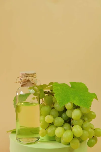 Traubenkernölflasche und grüne Trauben auf dem Podium auf beigem Hintergrund. Natürliches Bio-Traubenkernöl. — Stockfoto