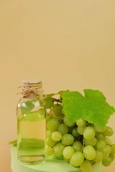 Traubenkernölflasche und Bündel grüner Trauben auf dem Podium auf beigem Hintergrund. Natürliches Bio-Traubenkernöl. — Stockfoto