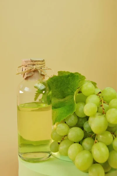 Aceite de semilla de uva.botella y racimo de uvas verdes en el podio. Aceite natural ecológico de semilla de uva Bio. —  Fotos de Stock