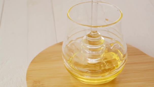 Miel en un palo de miel de vidrio. Miel líquida en un frasco de vidrio transparente con dipper.Palillo de vidrio para miel en una taza de vidrio sobre una mesa de madera. Miel fresca ecológica — Vídeo de stock