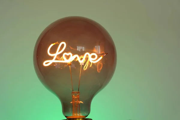 Láska. Žárovka s nápisem láska na smaragdovém pozadí. Valentýn. Symbol lásky. — Stock fotografie