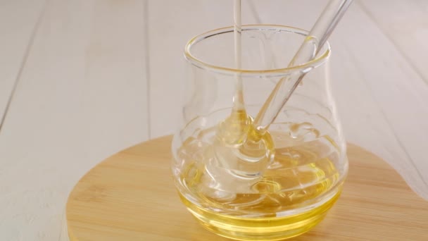 蜂蜜の棒に滴下します。透明ガラス瓶の中に蜂蜜を液体に浸した後、木のテーブルの上のガラスカップに蜂蜜のためのガラス棒。スローモーション。オーガニックフレッシュハニー — ストック動画