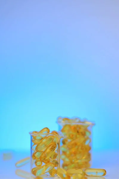 Fish oil capsules in glass laboratory flasks on a blue background.Omega 3 capsules. supplements and vitamins.omega fatty acids. Healthy eating and food supplements — Stock Photo, Image