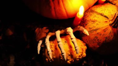 Karanlıkta mum ışığında balkabakları üzerinde iskelet parmaklar. Cadılar Bayramı sembolik arka planı. 4k görüntü