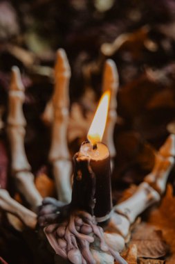 bone hand in crimson foliage with a candle.Candle Flame in Skeleton Hand for Halloween.Halloween creepy atmosphere. Halloween Candlestick. Halloween wallpaper with bone hand and candle. 