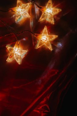 Kırmızı Kumaşta Parlayan Yıldız Dizisi Işıkları. Yıldız şekilli Peri Işığının Yakın Çekimi. Renkli arkaplanda yıldız şekilli iplik ışıkları. Parıldayan güzel noel duvar kağıtları.