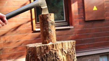Adam sokağın ortasında baltayla tahta bir evin arka planına odun kesiyor. Katı ısıtma yakıtı. Isıtma mevsimi için odun hazırlıyorum. Doğal ısı kaynağı ve evin ısıtması. 4k görüntü