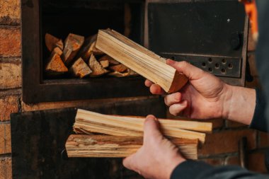 Isıtma mevsimi. Brick Oven 'a odun eken adam. Bir adamın elleri şömineye bir kucak dolusu doğranmış odun koyar. Katı doğal ısıtma yakıtı..