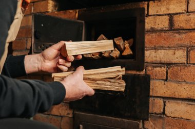 Brick Oven 'a Odun Ekleyen Adam. Bir adamın elleri şömineye bir kucak dolusu doğranmış odun koyar. Katı doğal ısıtma yakıtı..