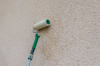 Bej ve gri tonlarda bir ev boyamak. İnşaat ve yenileme kavramı. Dekoratör, silindirle duvar boyuyor.