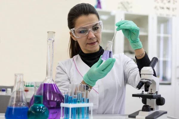 A female chemist in protective glasses conducts a study of the substance in a flask in the laboratory. The chemist mixes the solution in the flask