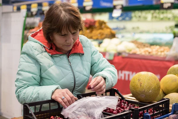 A woman in a grocery store chooses fresh vegetables and fruits. Buying fruits and vegetables in the supermarket