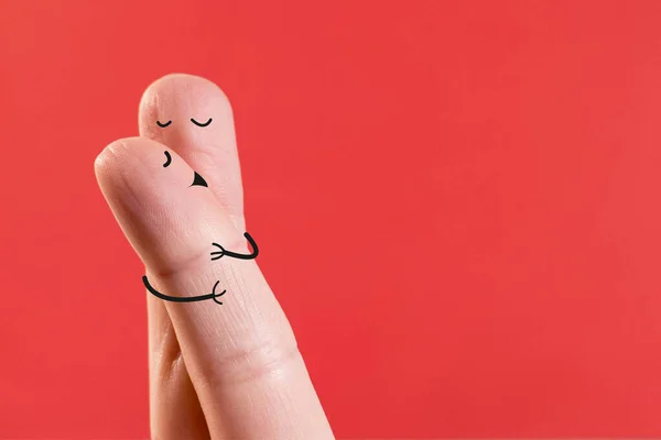 Happy couple in love with painted smiley and hugging and kissing. Two fingers with faces drawn on them kissing on a red background. Copy space.  Valentine\'s Day.