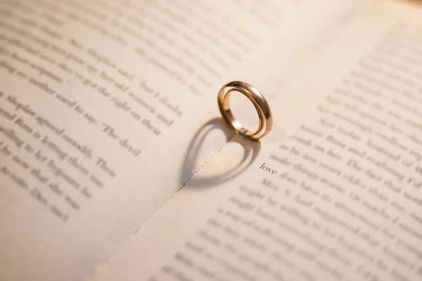 Two wedding rings on an open book near the word love. Two rings cast a shadow in the form of a double heart. Signs and symbols of love.